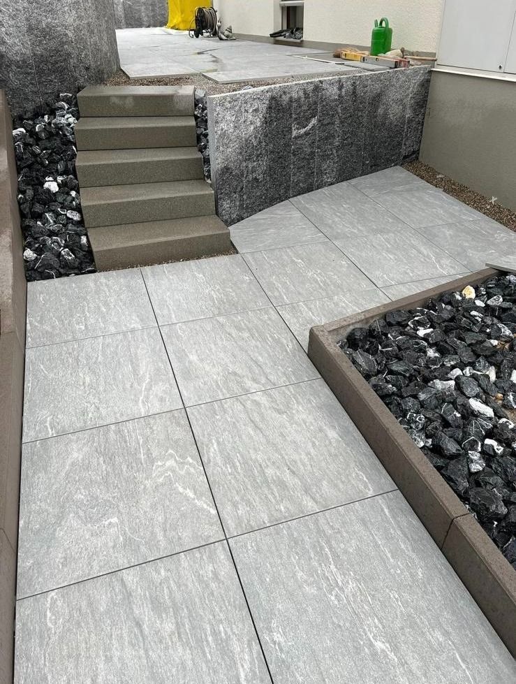 Ein Betonweg mit Treppen und einem mit Steinen gefüllten Blumenkasten.