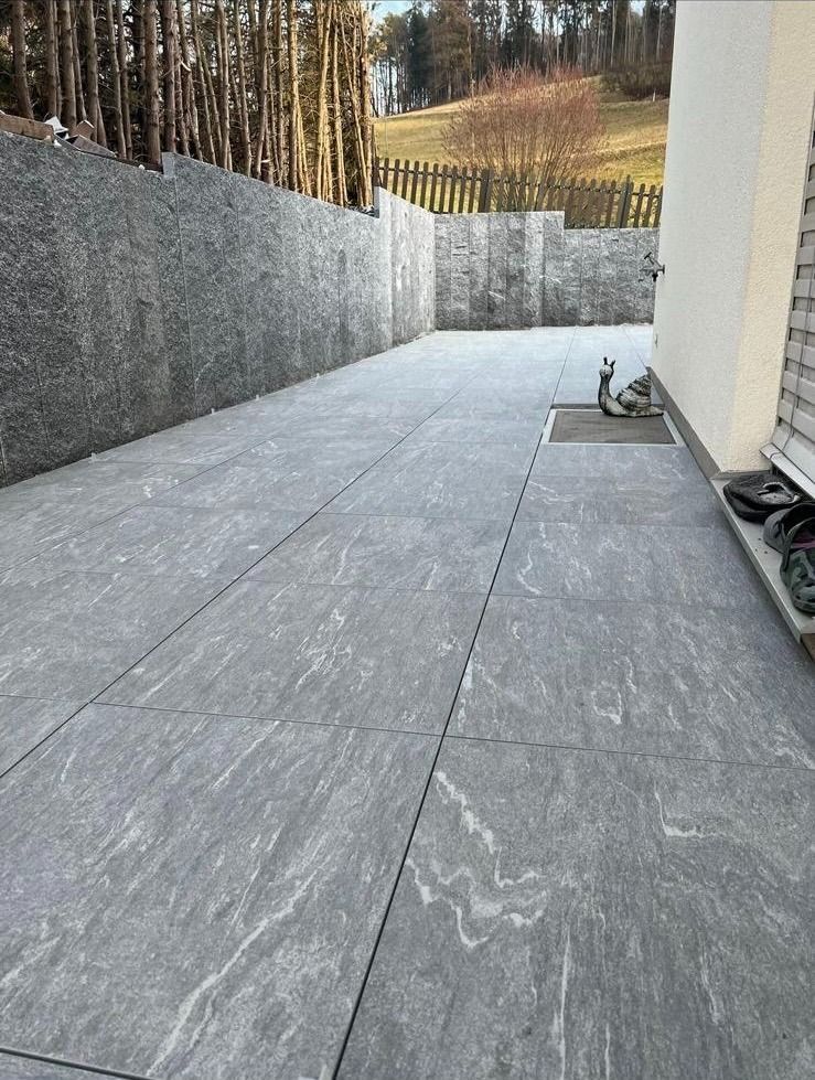 Eine Terrasse mit einem Zaun und Bäumen im Hintergrund.