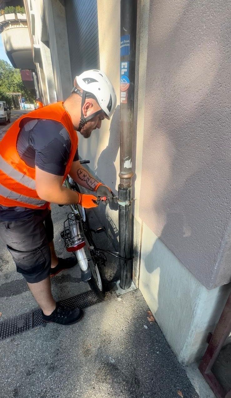 Ein Mann mit Helm und orangefarbener Weste arbeitet an einem Fahrrad.