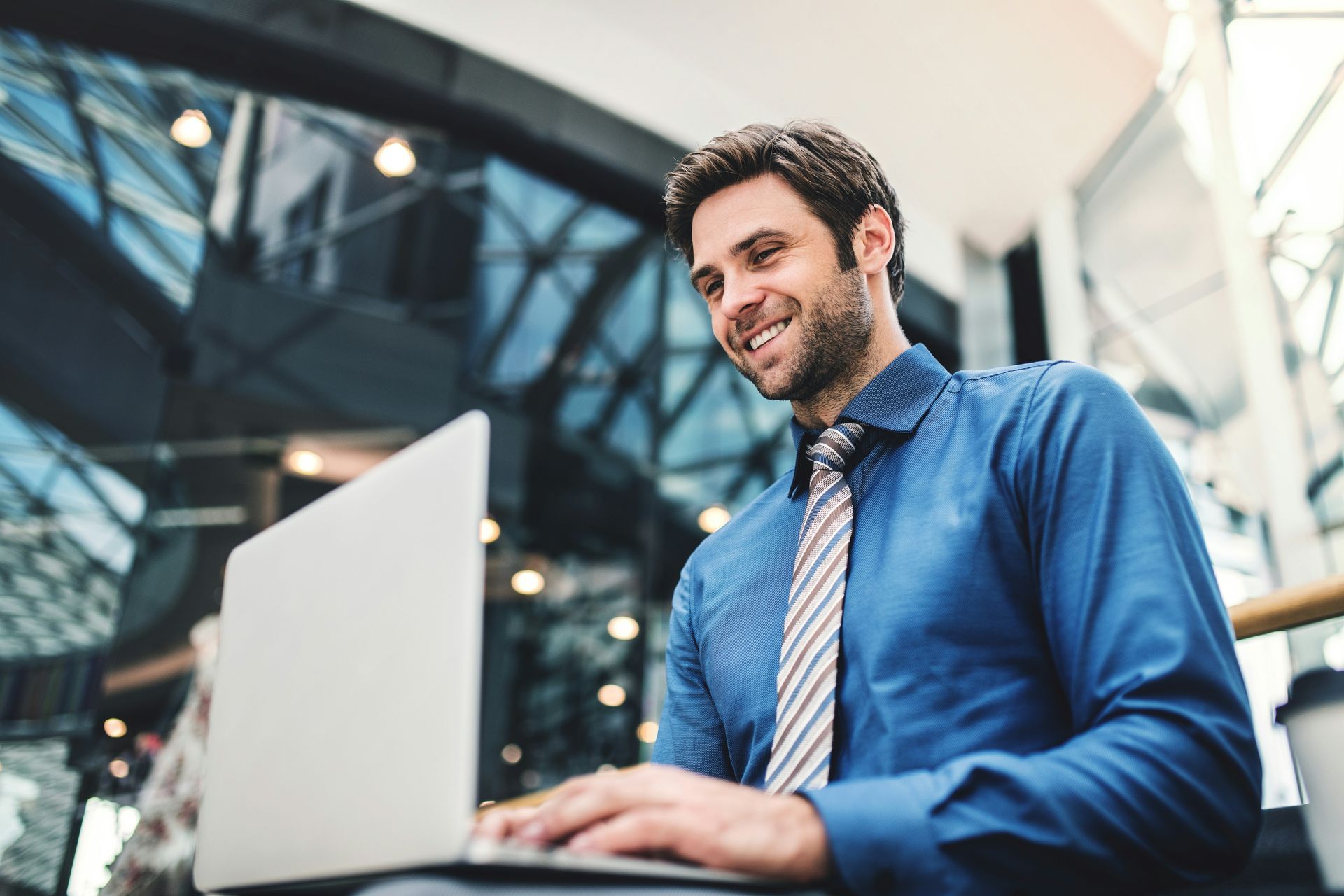 A man in a blue shirt and tie is using a laptop computer.