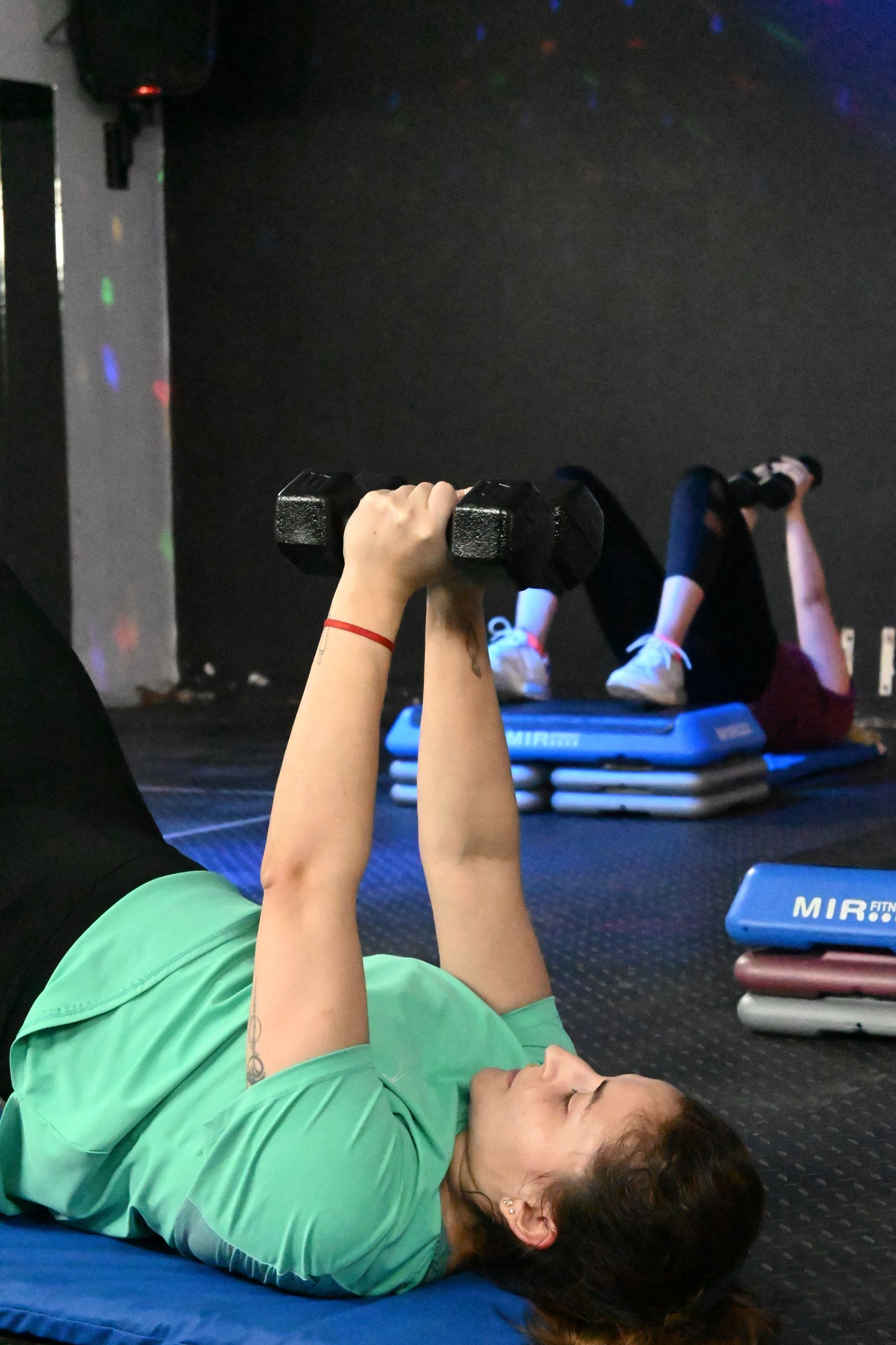 Una mujer con una camisa verde está levantando una mancuerna en un gimnasio.
