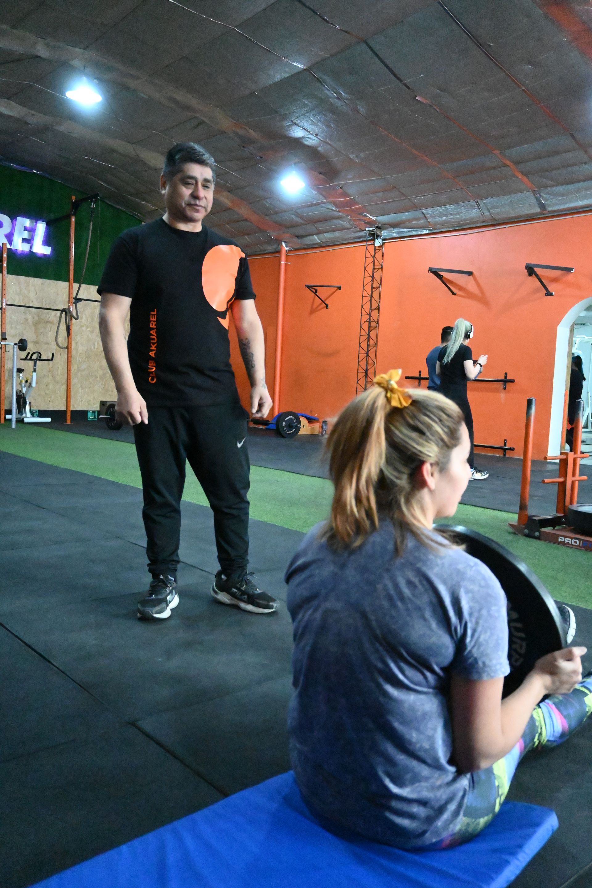Un hombre está de pie junto a una mujer sentada en un banco en un gimnasio.