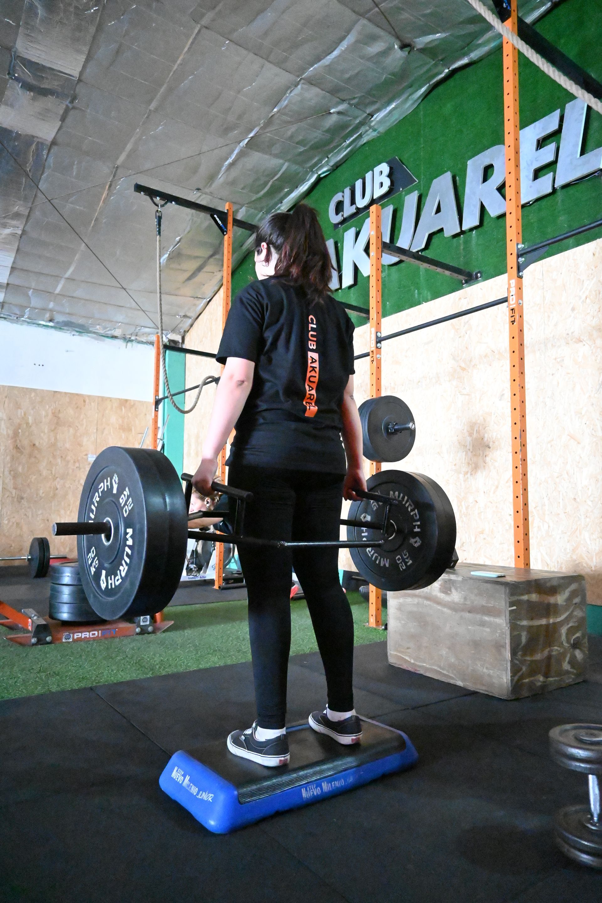 Una mujer está de pie en una plataforma sosteniendo una barra en un gimnasio.