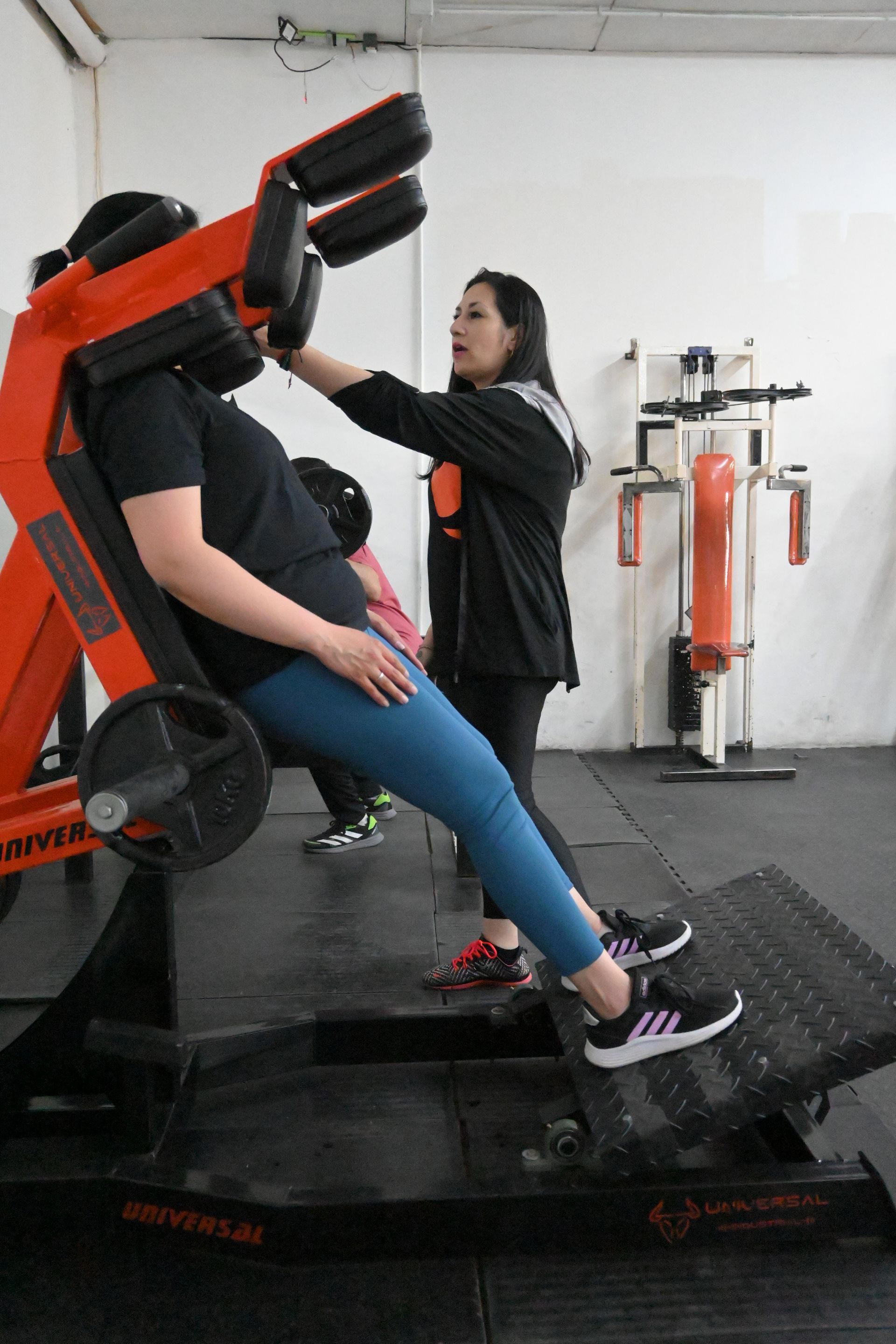 Una mujer está sentada en una máquina en un gimnasio mientras otra mujer observa.