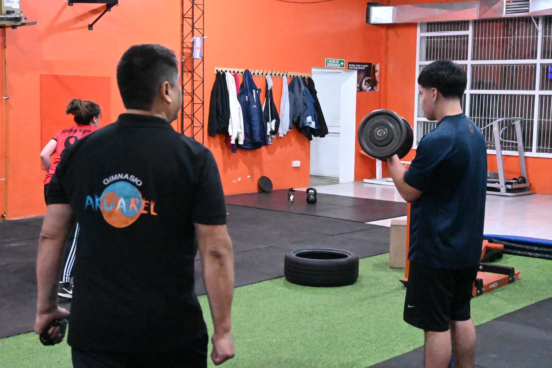 Dos hombres están de pie en un gimnasio mirando una mancuerna.