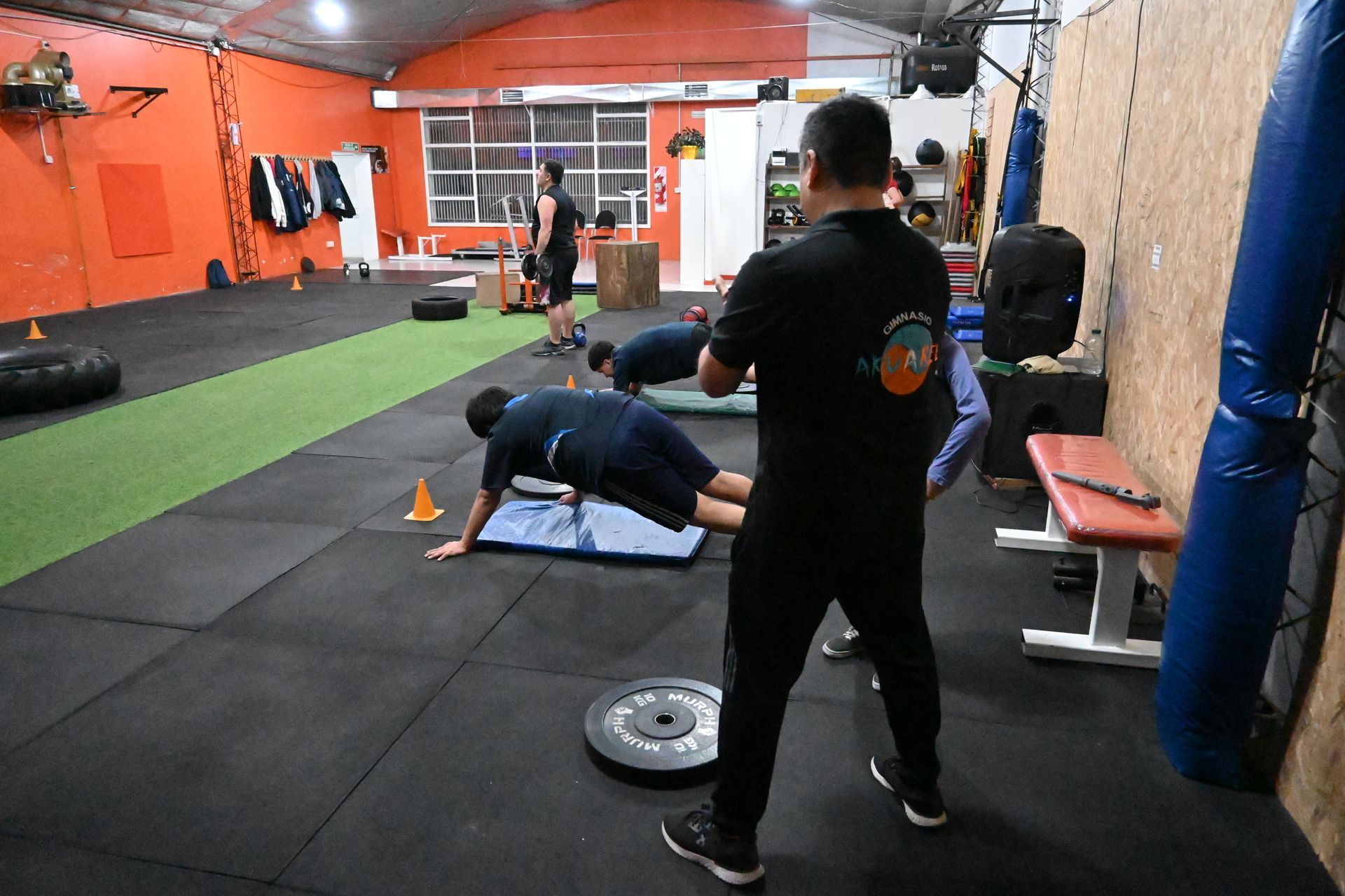 Un hombre está parado frente a un grupo de personas haciendo flexiones en un gimnasio.