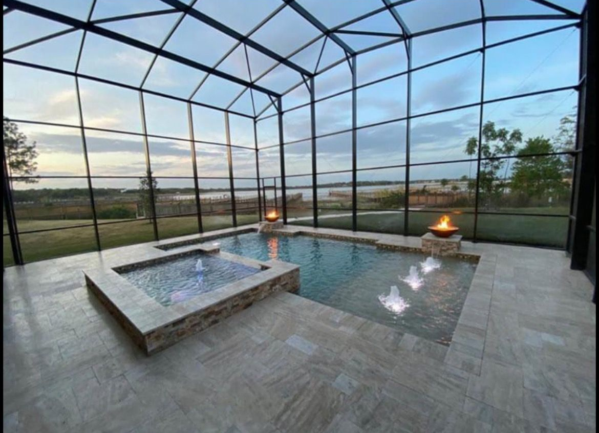 Pool enclosure attached to a house, with a pool visible inside. Green grass and trees are in the background.