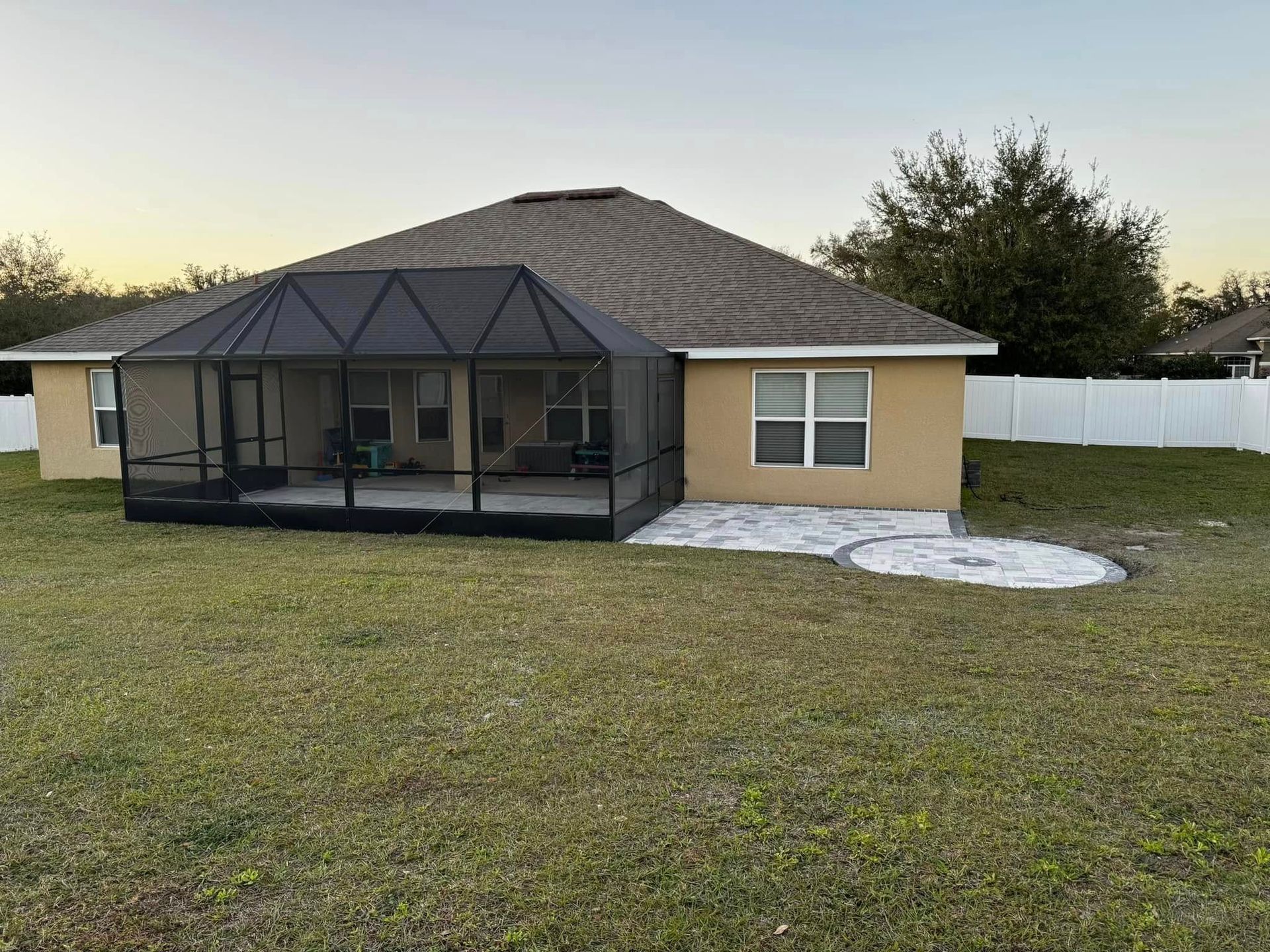 Screened-in patio attached to a white house with green lawn and bushes; overcast sky.