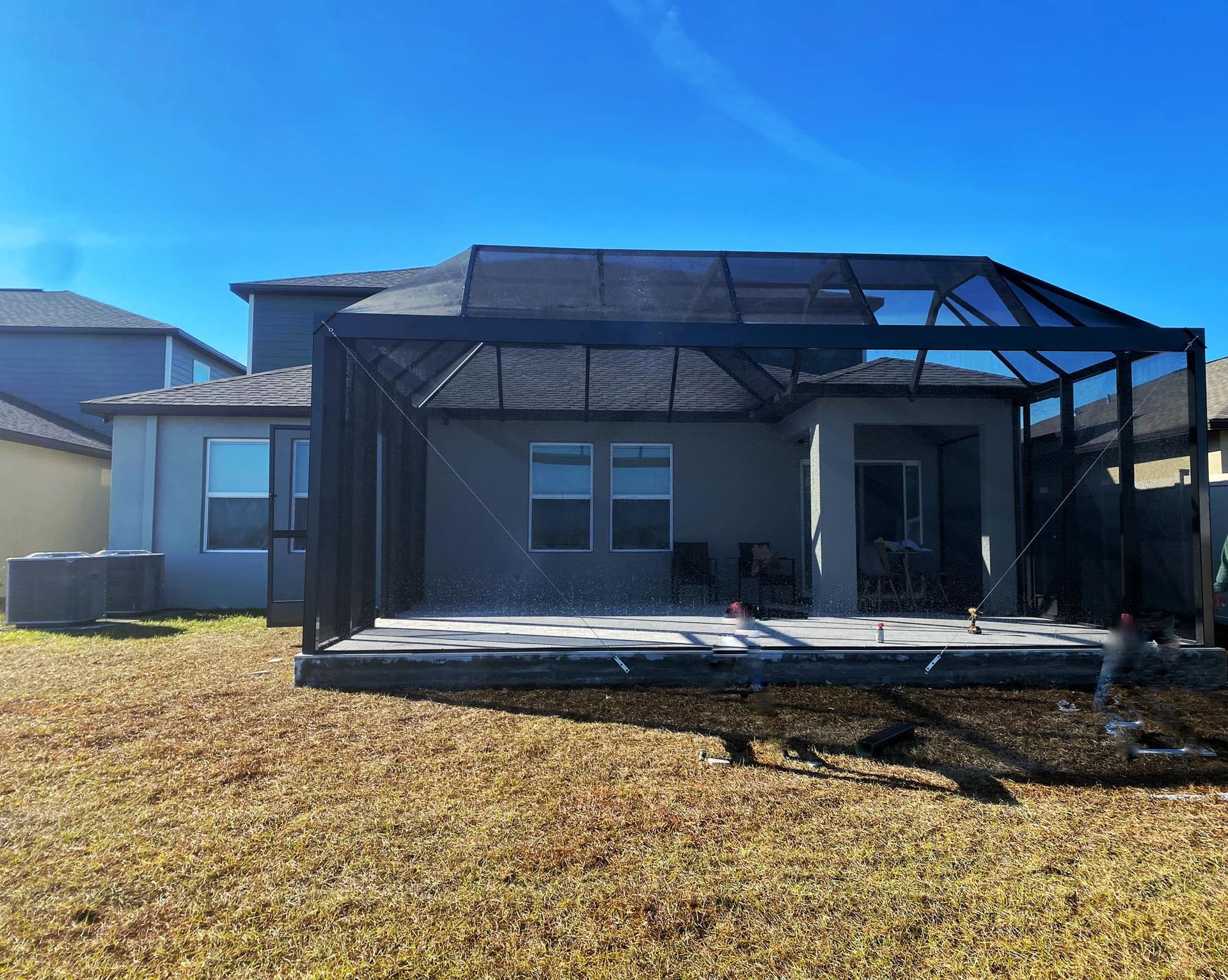 Backyard view of a house with a screened-in patio, brown grass, and a bright blue sky.