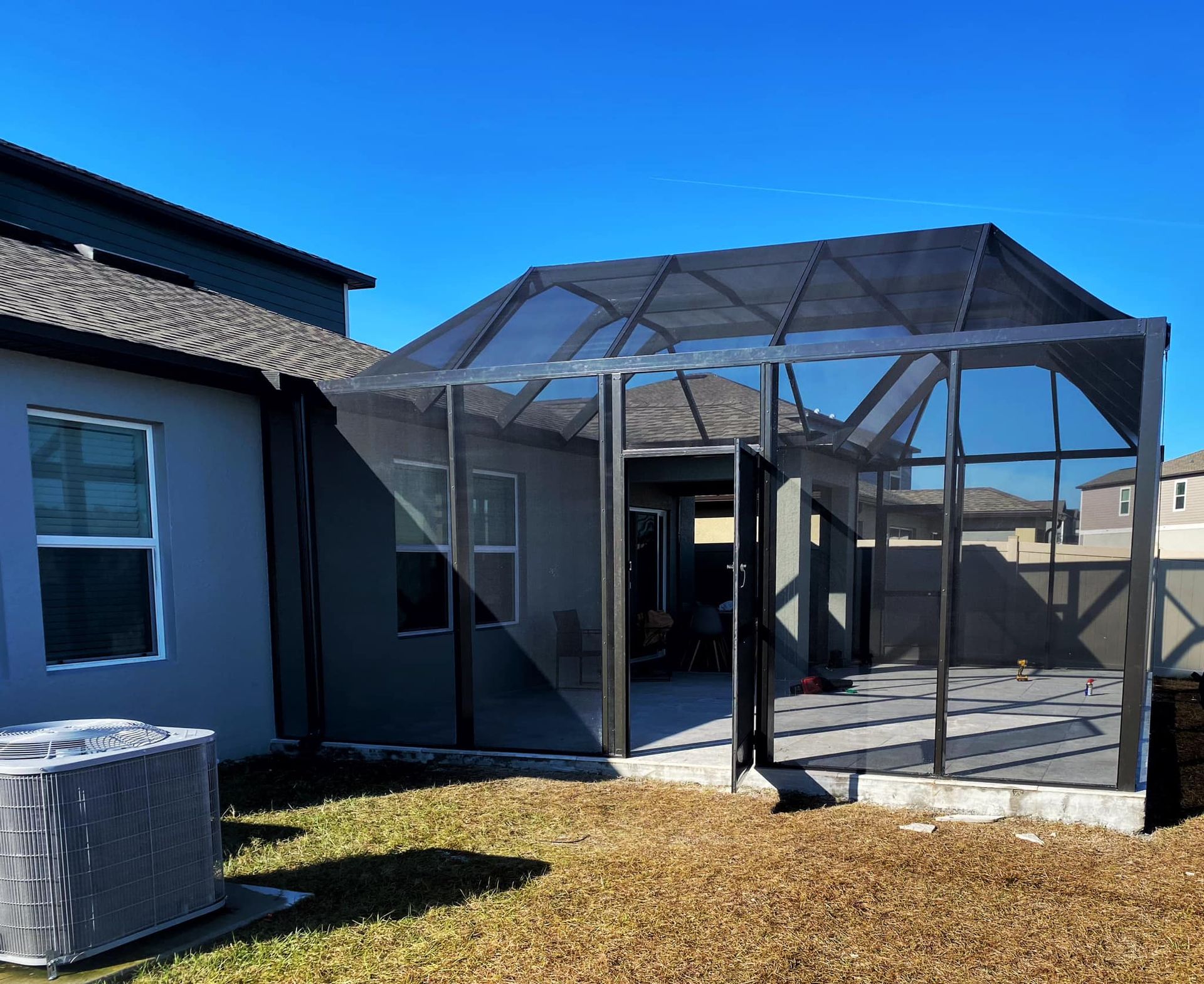Screened patio enclosure attached to a gray house with a clear blue sky.