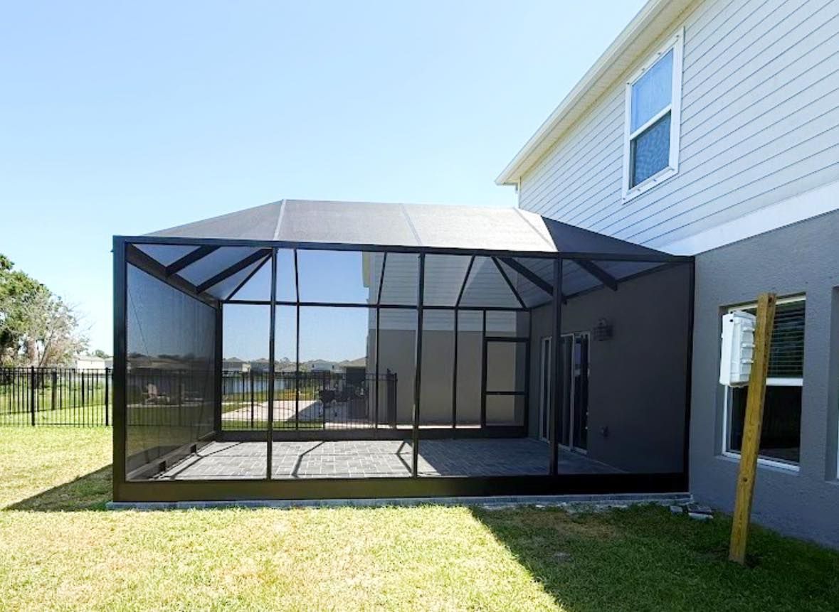 Black-screened patio enclosure attached to a two-story gray house on a sunny day.