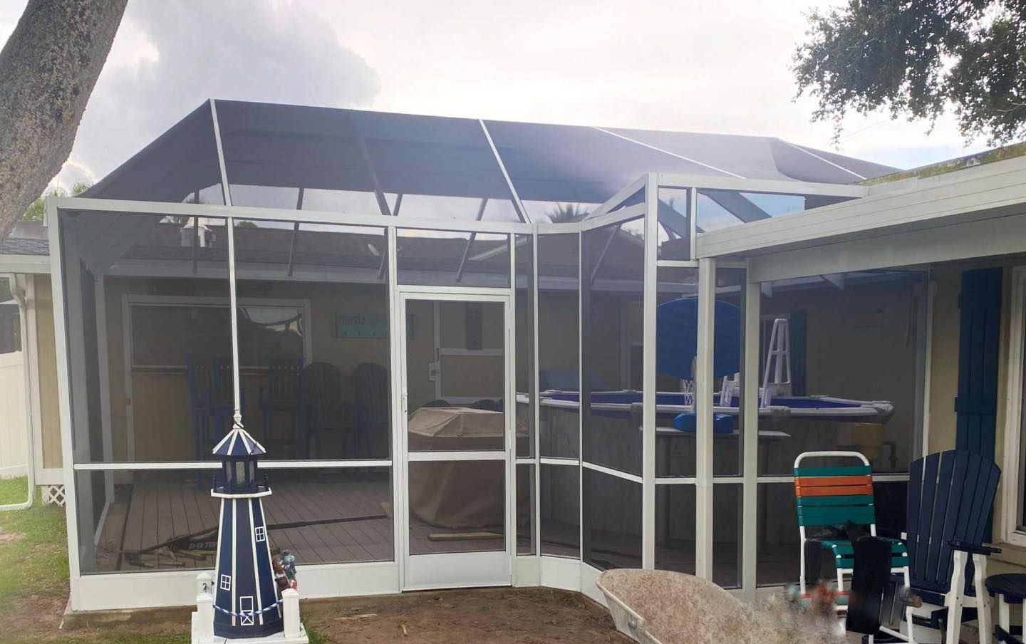 White screened-in pool enclosure attached to a beige house; teal and white chairs nearby.