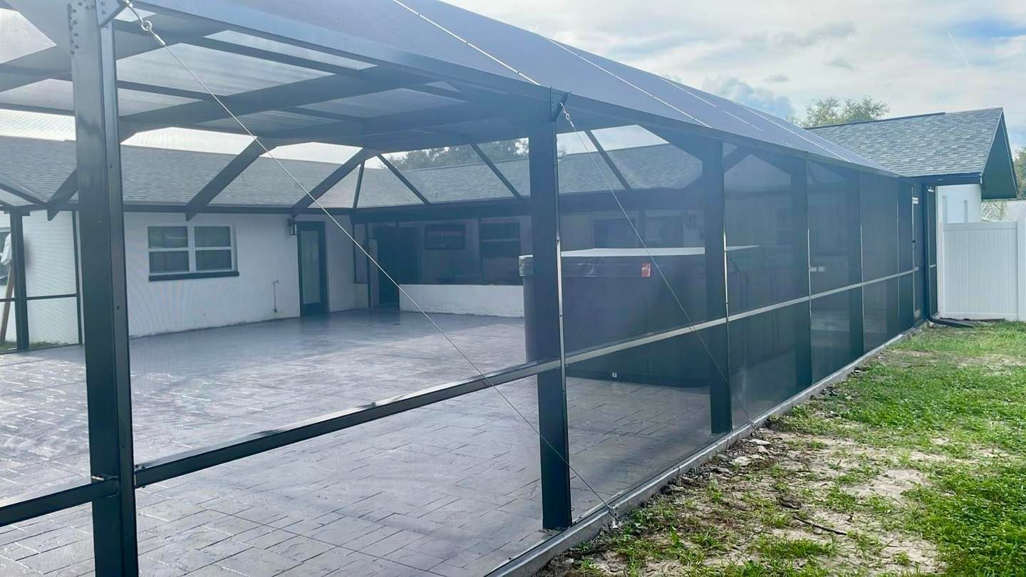 Screened-in patio with dark frames, gray floor, and white house. Green grass and white fence on the right.