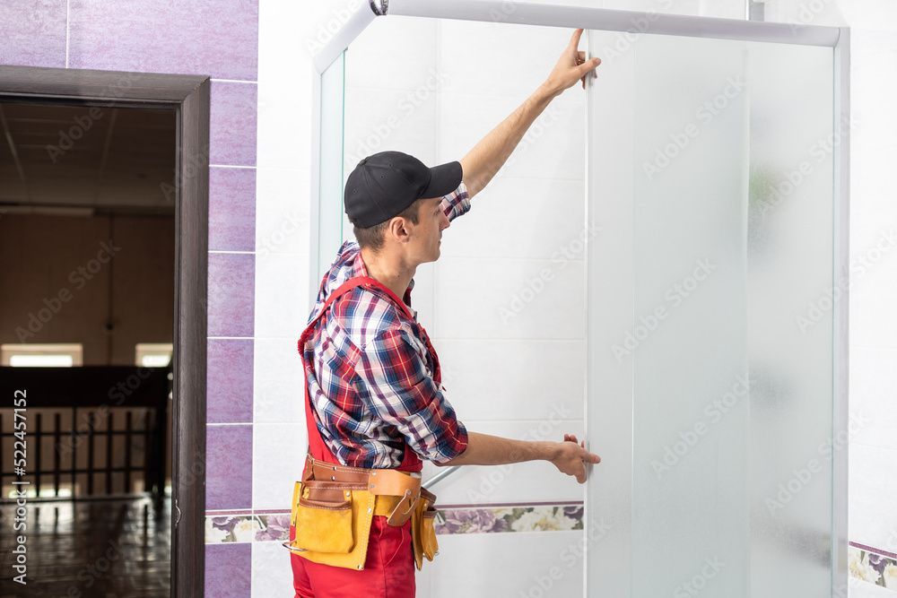 A young man repairing the door of the shower cabin in the bathroom.