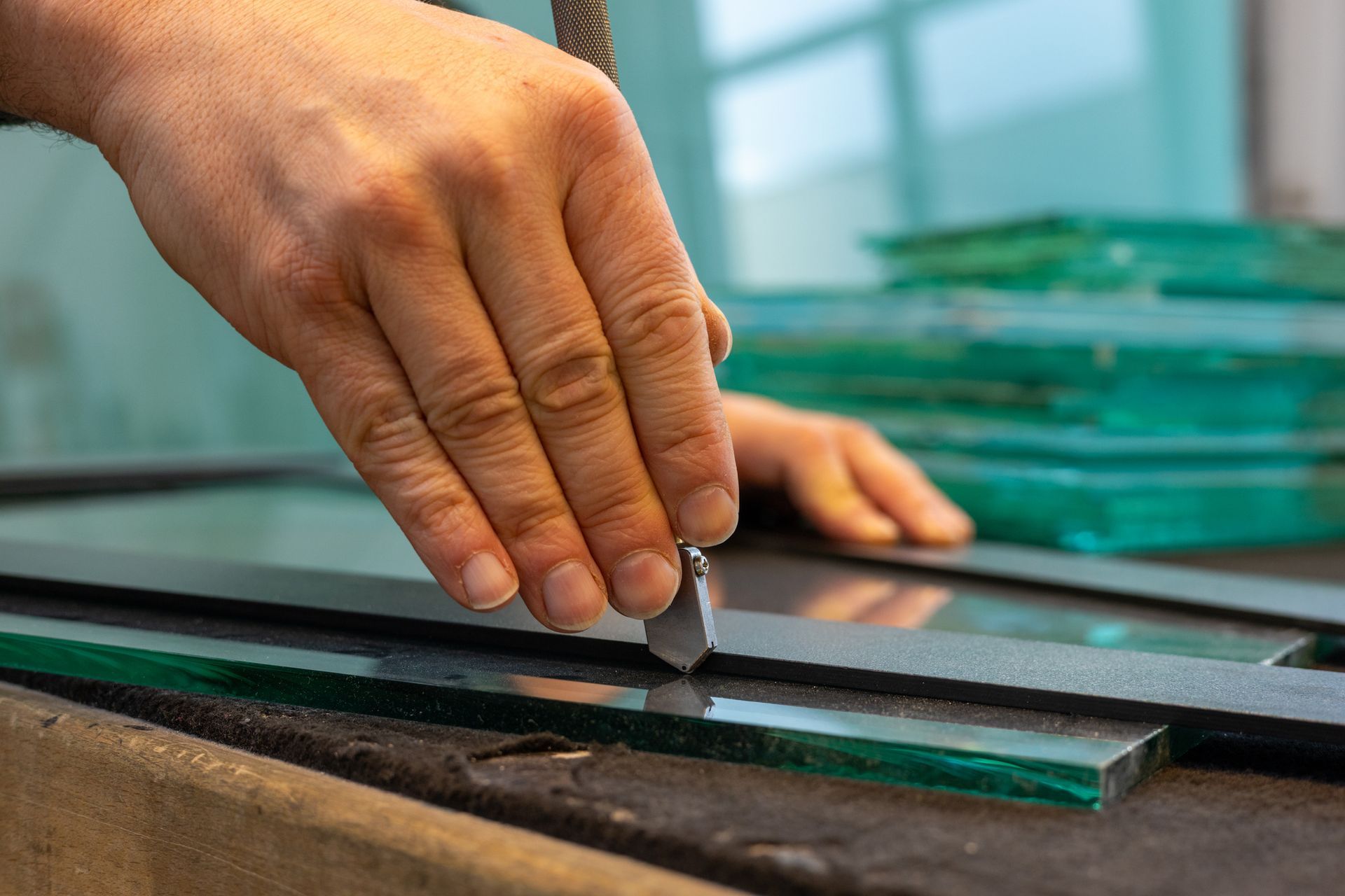 A hand uses a glass cutter on top of a table, inside a glass factory.