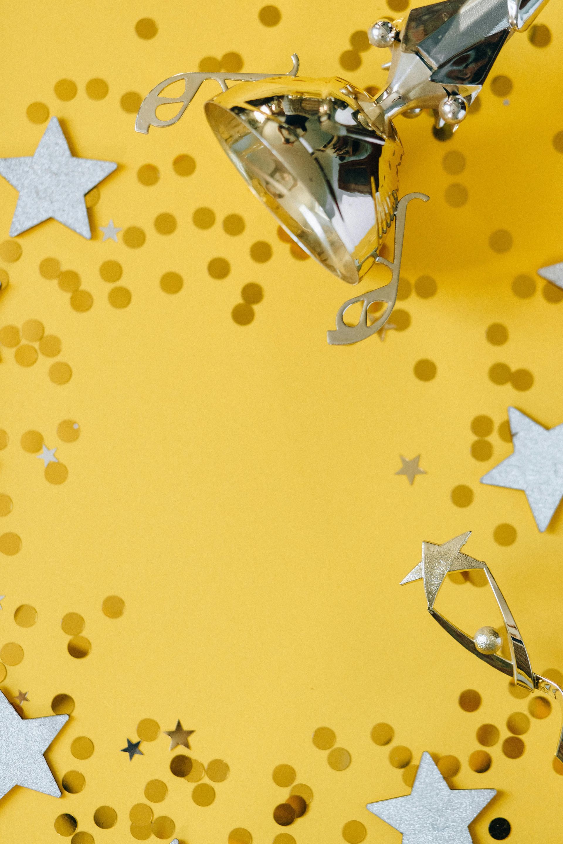 A trophy is surrounded by confetti and stars on a yellow background.