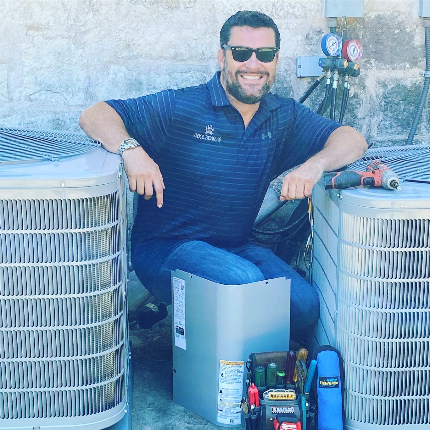 A man wearing sunglasses is sitting next to two air conditioners