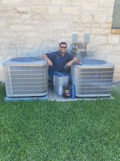 A man is sitting on the ground next to two air conditioners.