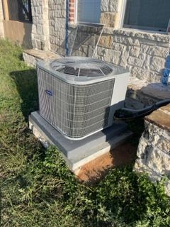 A large air conditioner is sitting in the grass in front of a brick building.