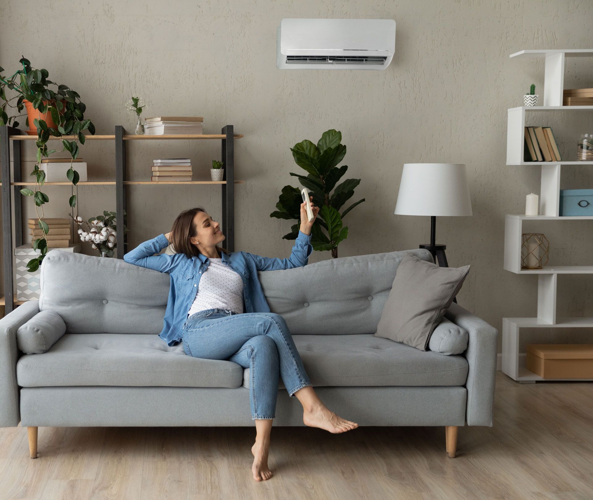 A woman is sitting on a couch in a living room holding a remote control.