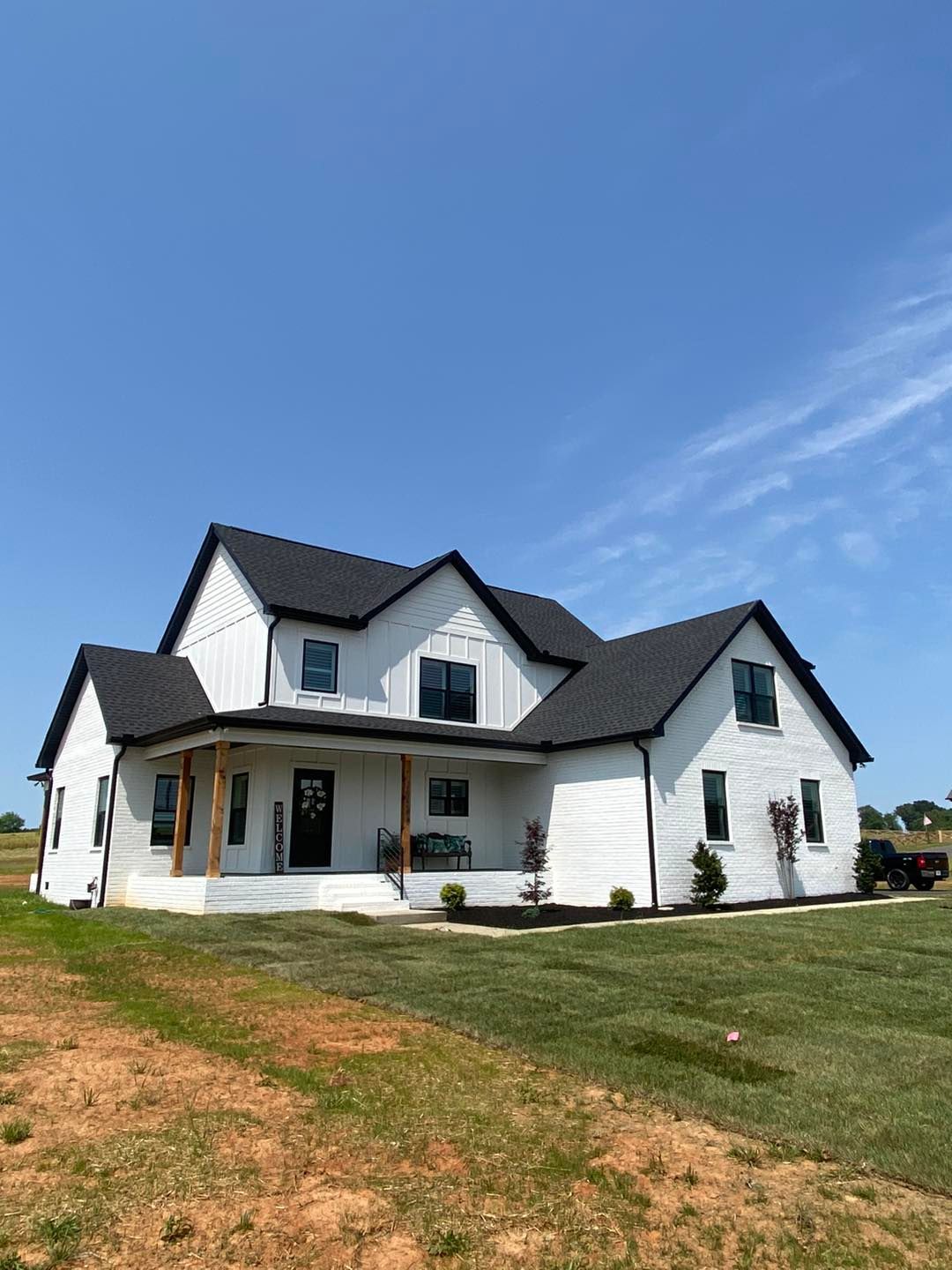A large white house with a black roof is sitting on top of a lush green field.