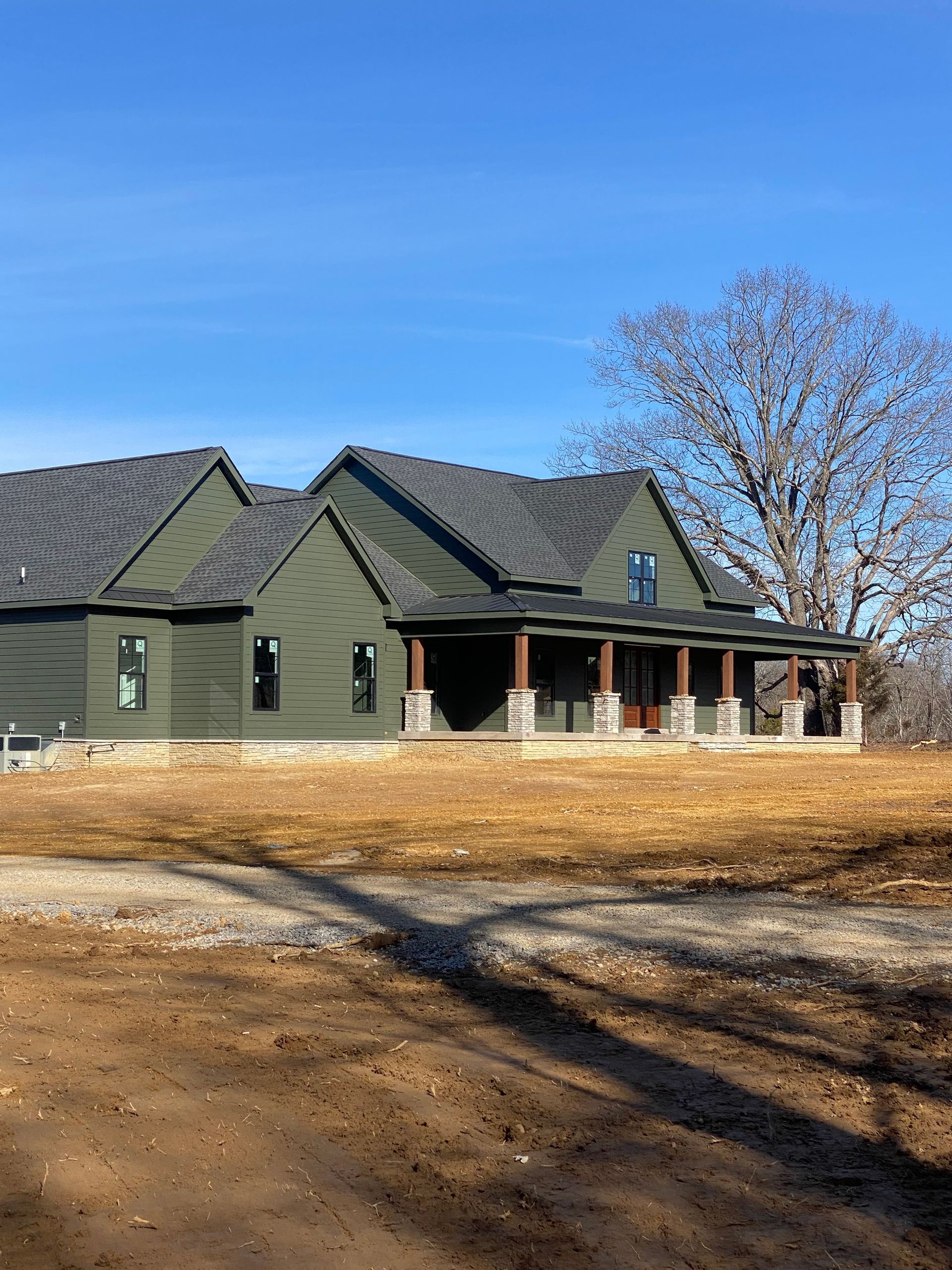 A large green house with a porch is sitting on top of a dirt field.