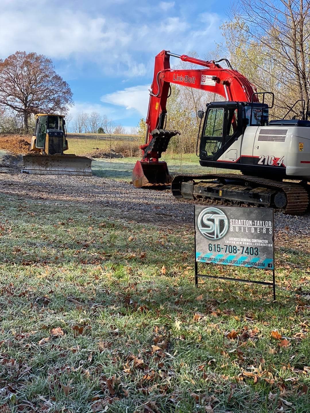 A large excavator is parked in a grassy field next to a sign.