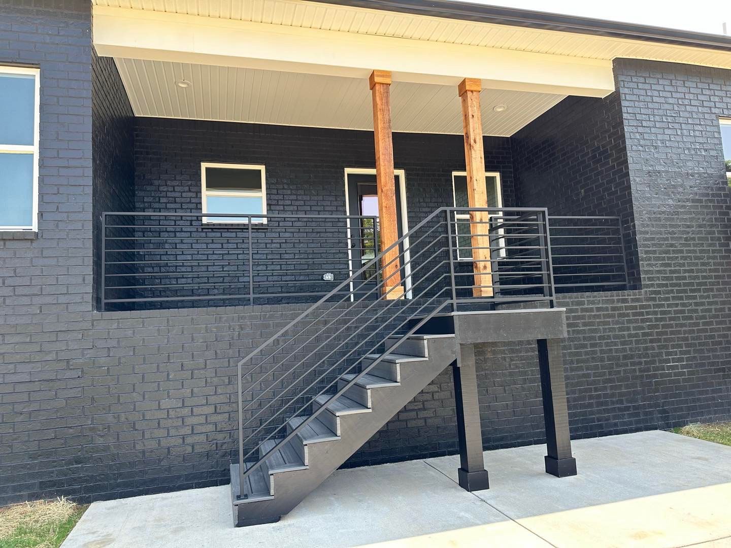 A black brick house with stairs leading up to the front porch.