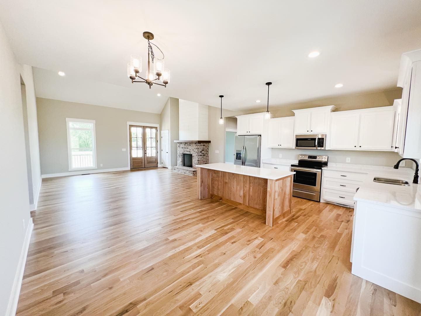 A kitchen with hardwood floors , white cabinets and stainless steel appliances.