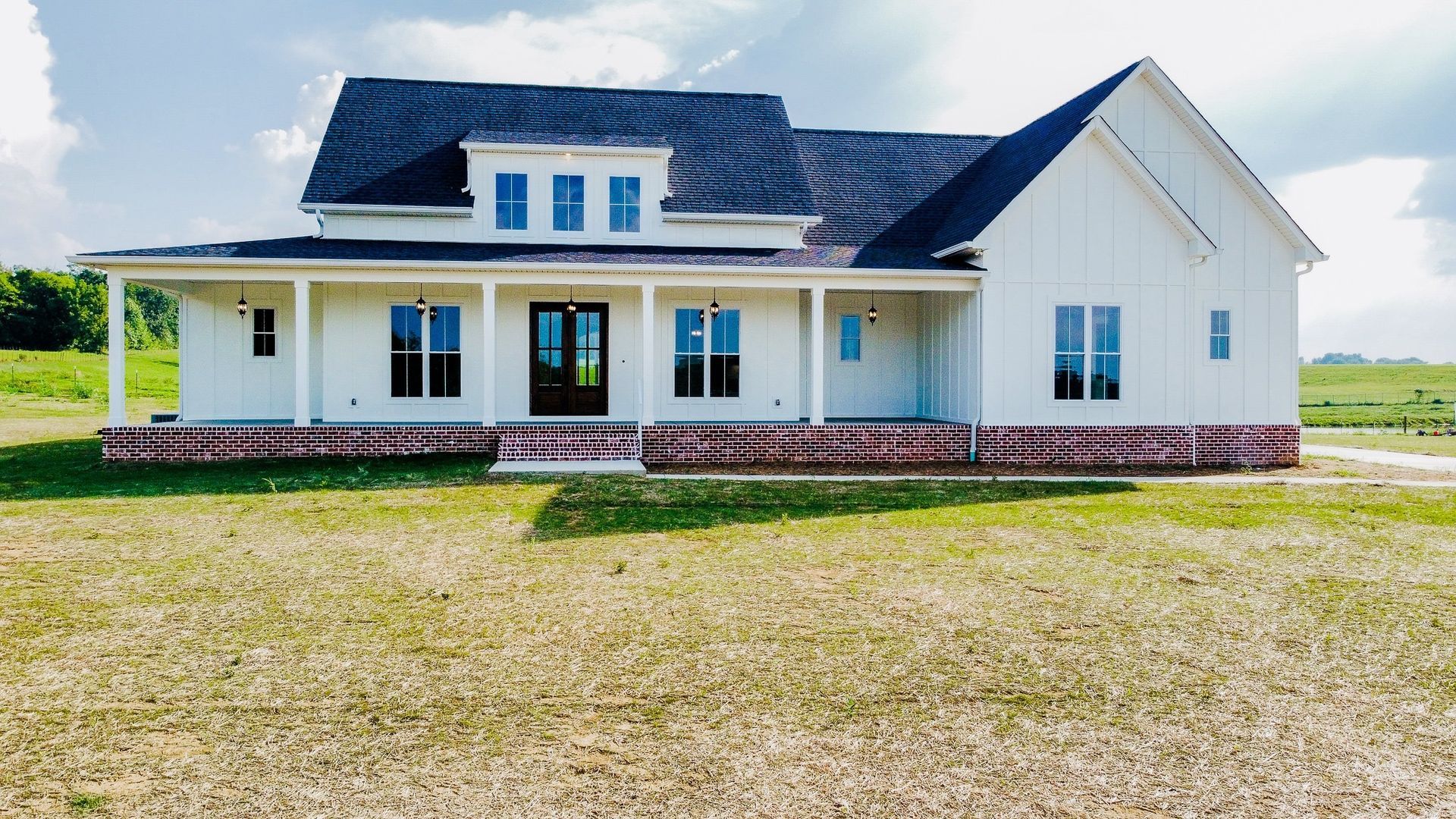 A white house with a black roof is sitting in the middle of a grassy field.