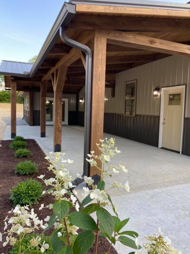 A building with a covered porch and flowers in front of it.