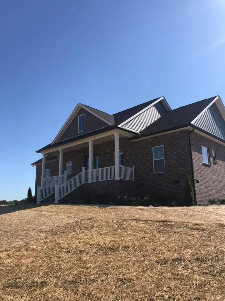 A large brick house with a large porch is sitting on top of a hill.
