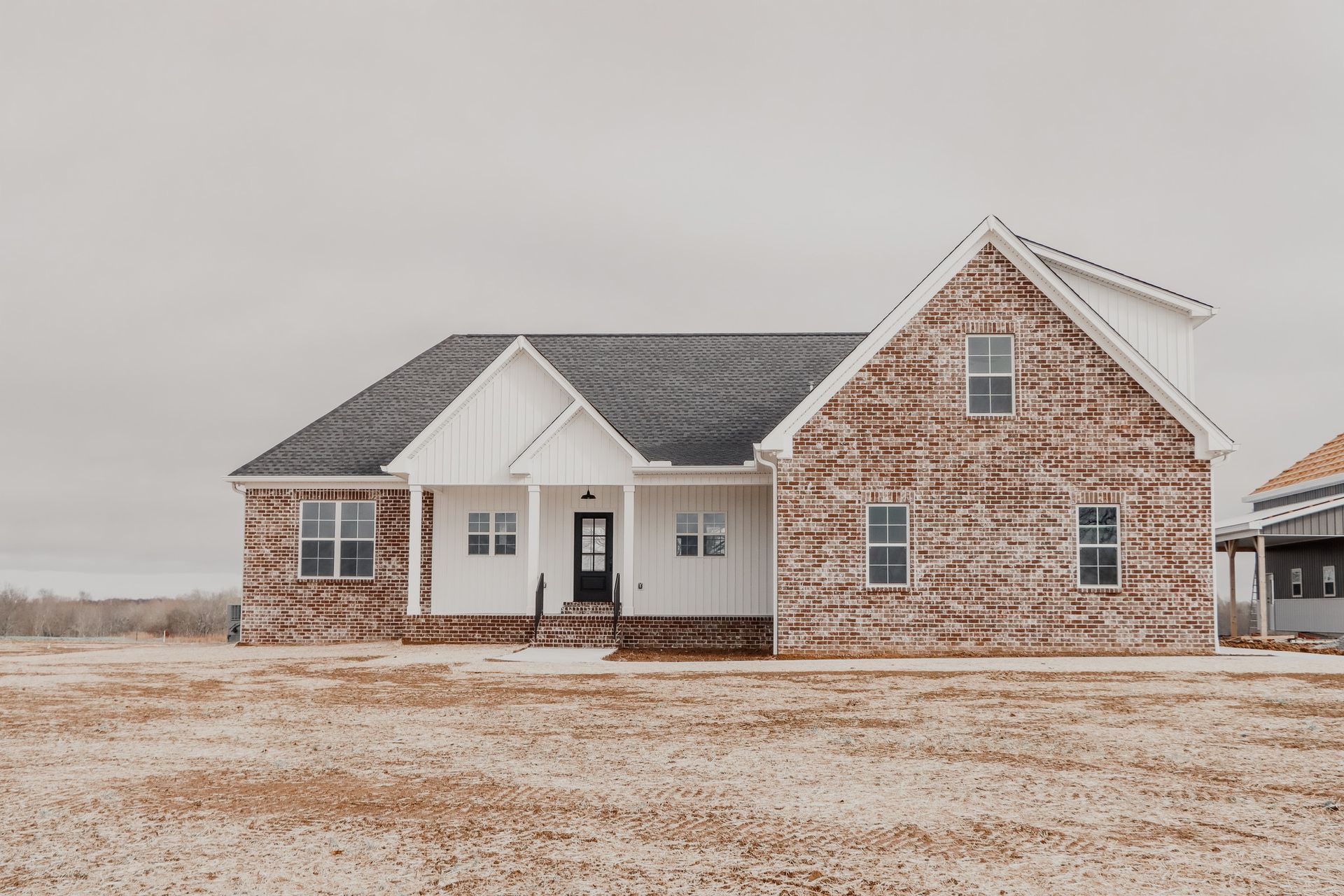 A large brick house with a black roof is sitting in the middle of a field.