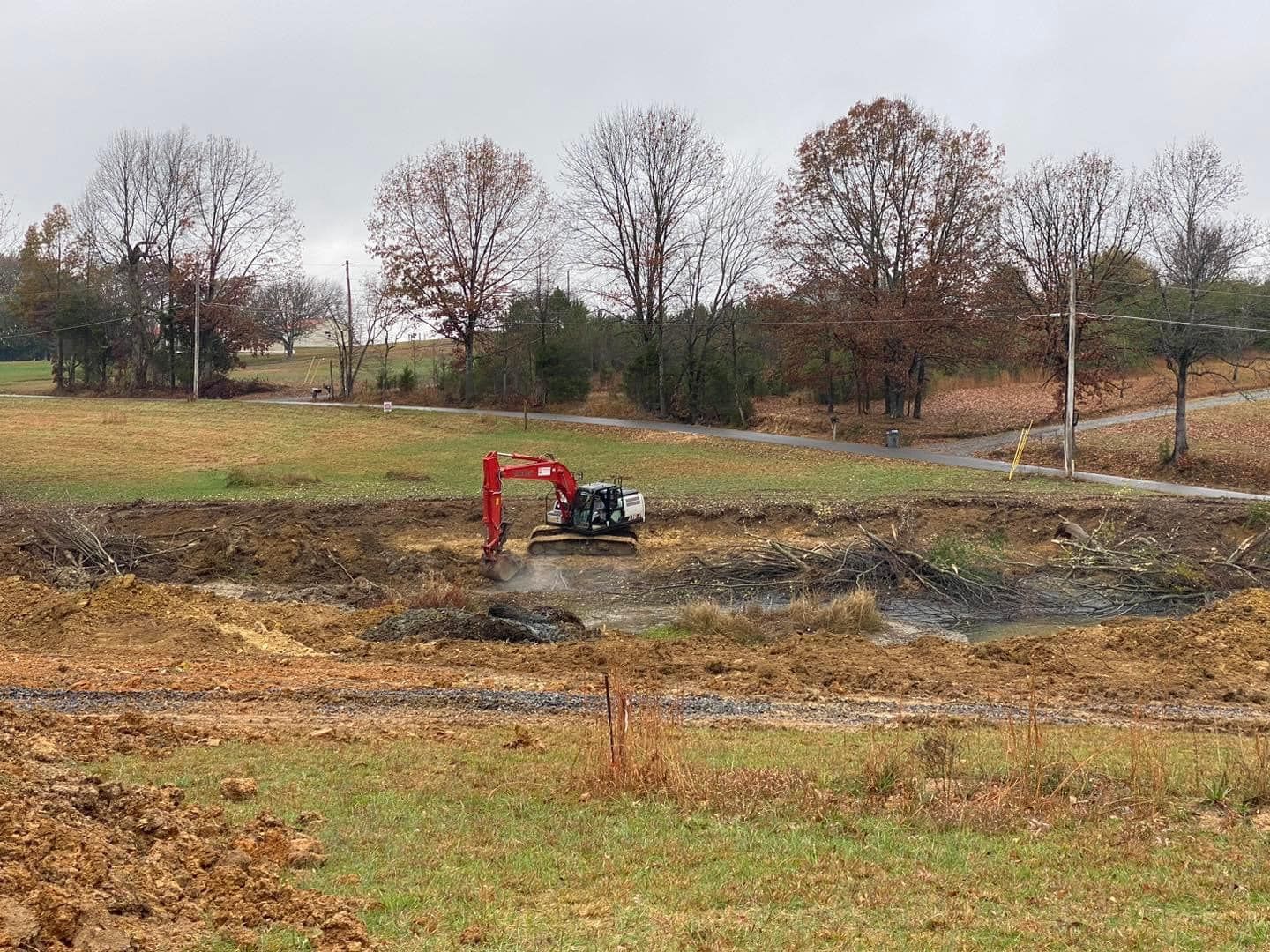A red excavator is digging a hole in a field.