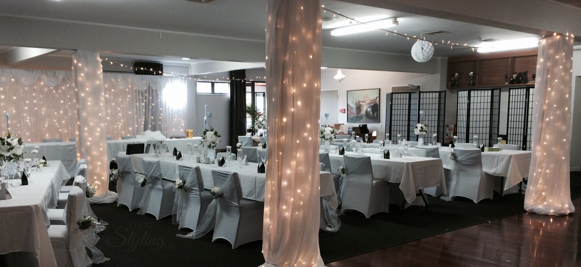 Fairy light and fabric dressed pillars with white fairy curtain backdrop by Event Styling Co for an Auckland wedding.
