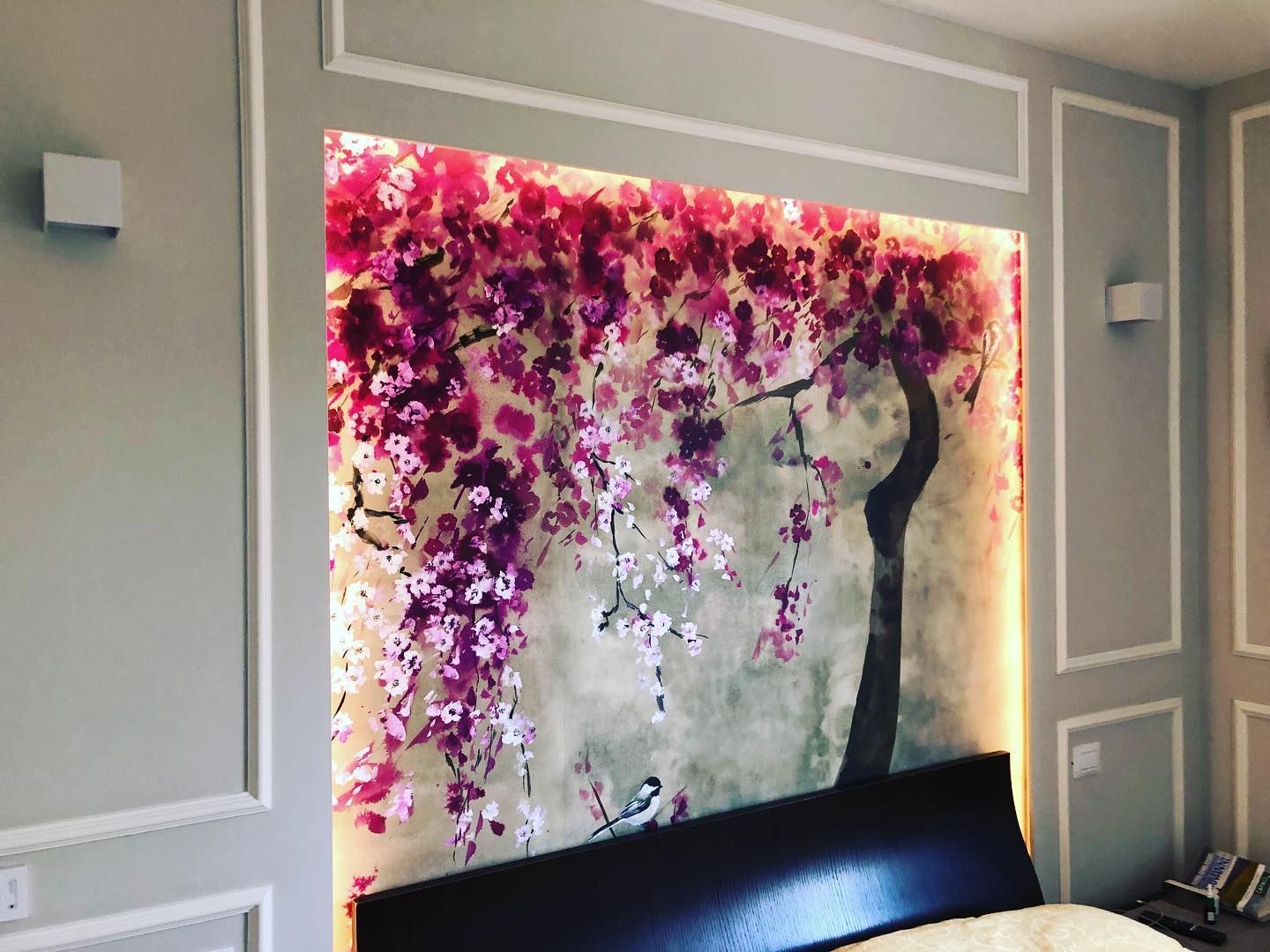 Una nicchia nella parete della camera da letto con un murale raffigurante fiori di ciliegio, illuminato da luci soffuse.