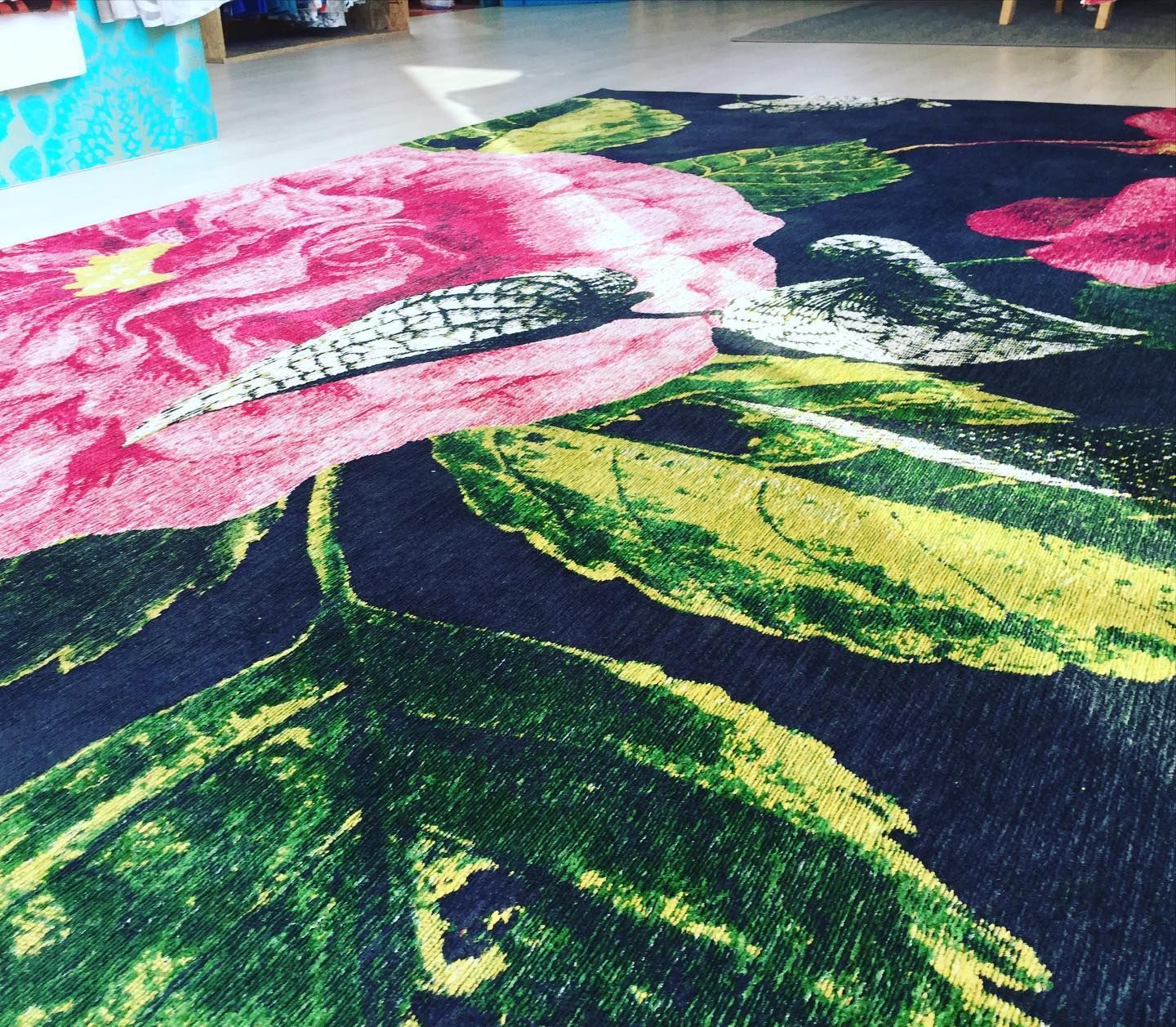 Primo piano di un tappeto floreale con grandi fiori rosa, foglie verdi e uno sfondo blu navy.