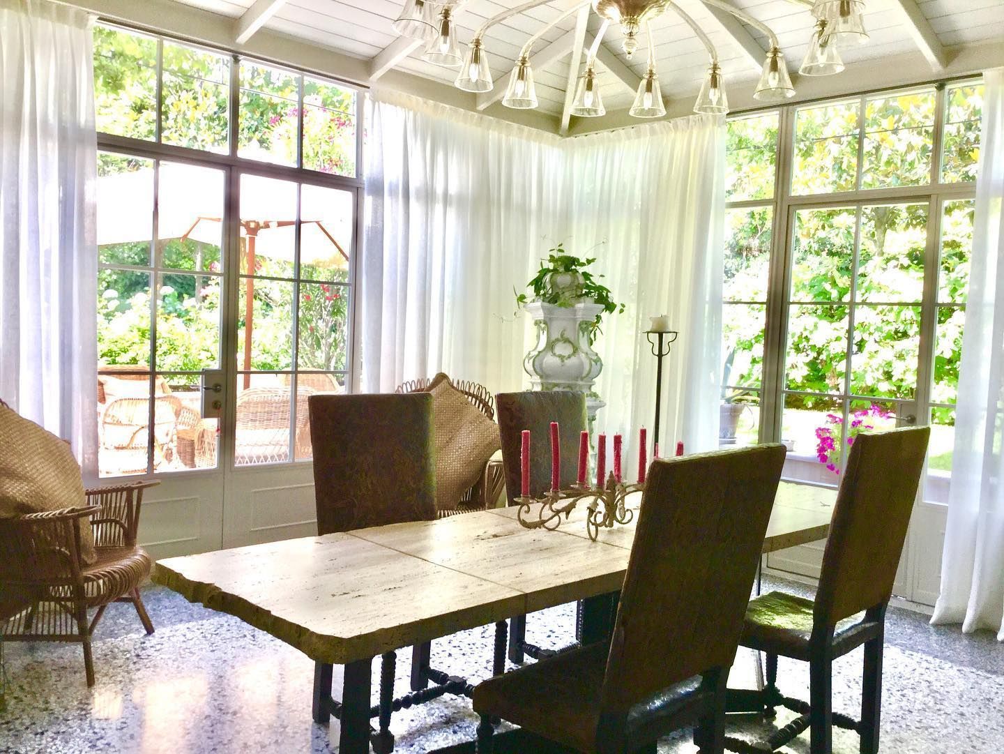 Sala da pranzo soleggiata con lungo tavolo in marmo, sedie marroni e tende bianche. L'esterno è visibile attraverso le finestre.