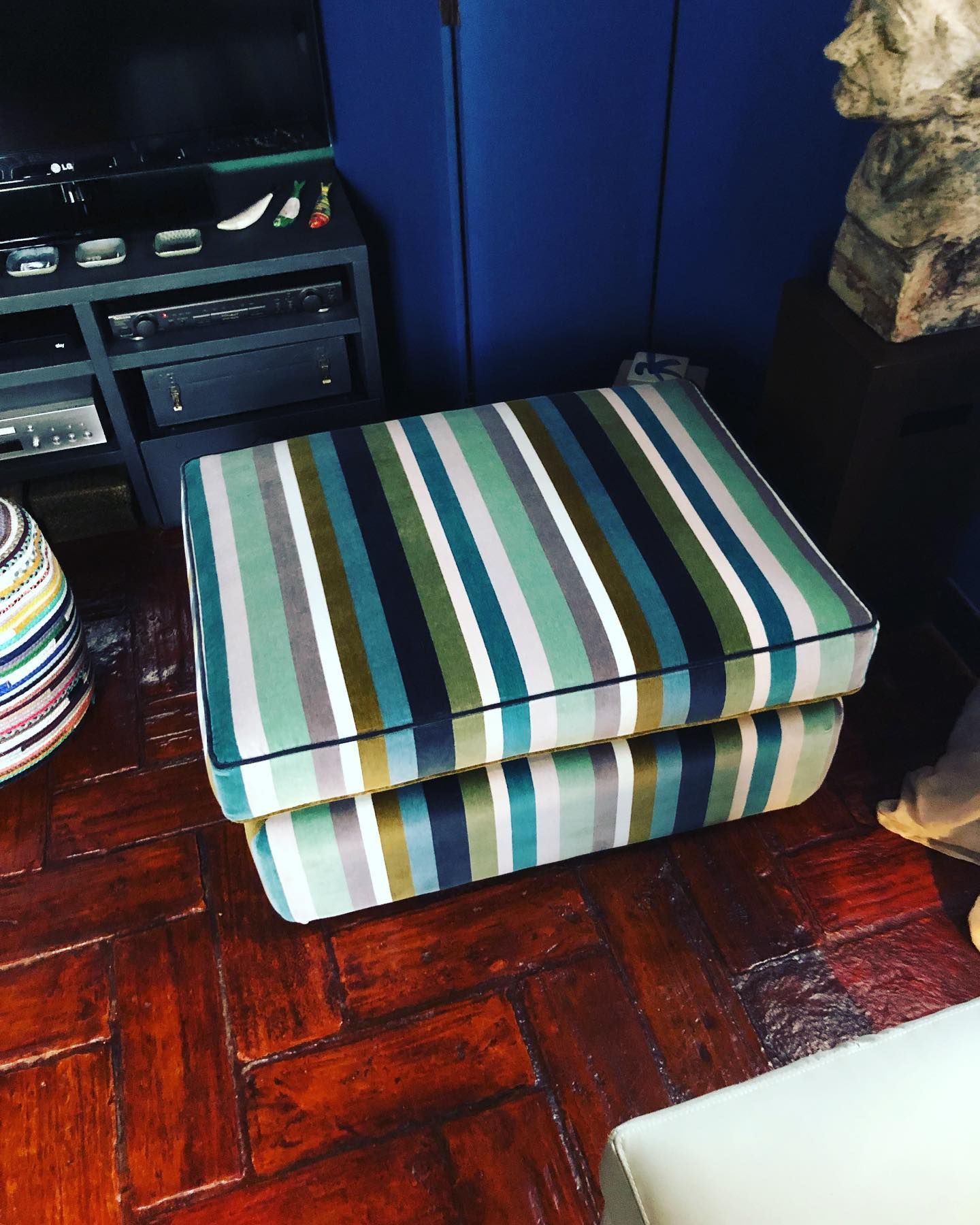 Pouf a righe su un pavimento in legno, vicino a un mobile blu e a un mobile porta TV.