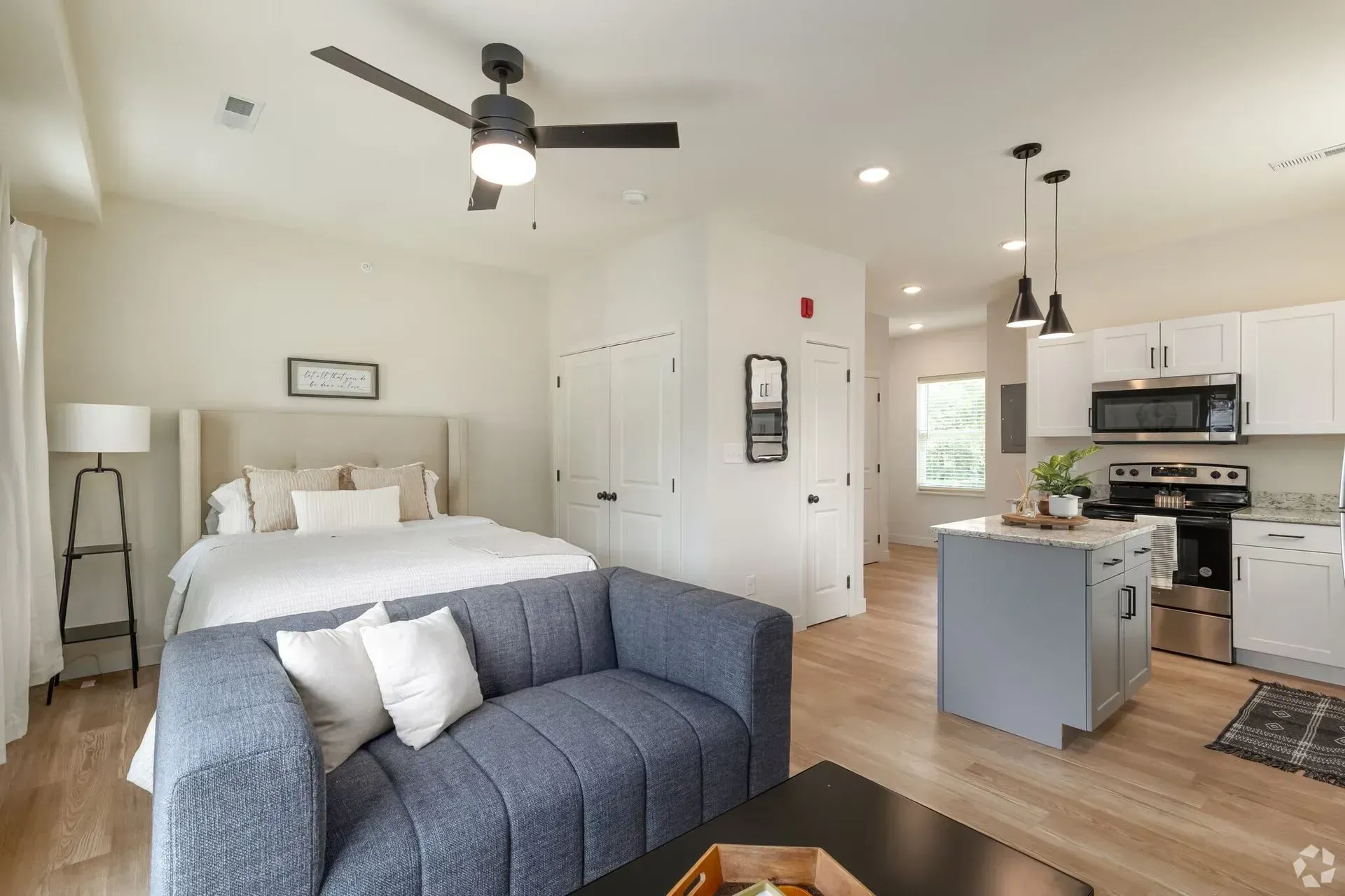Modern Millcreek studio with open layout featuring bed, blue sofa, stainless steel kitchen appliance