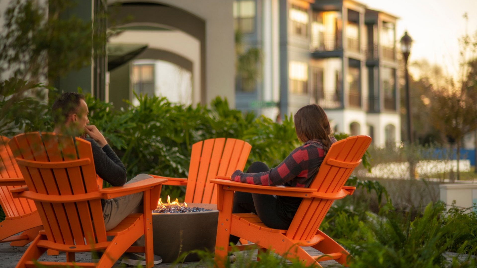 Young couple sitting in orange Adirondack chairs by a fire pit in the amenities area at the Central on Orange Lake Apartments 