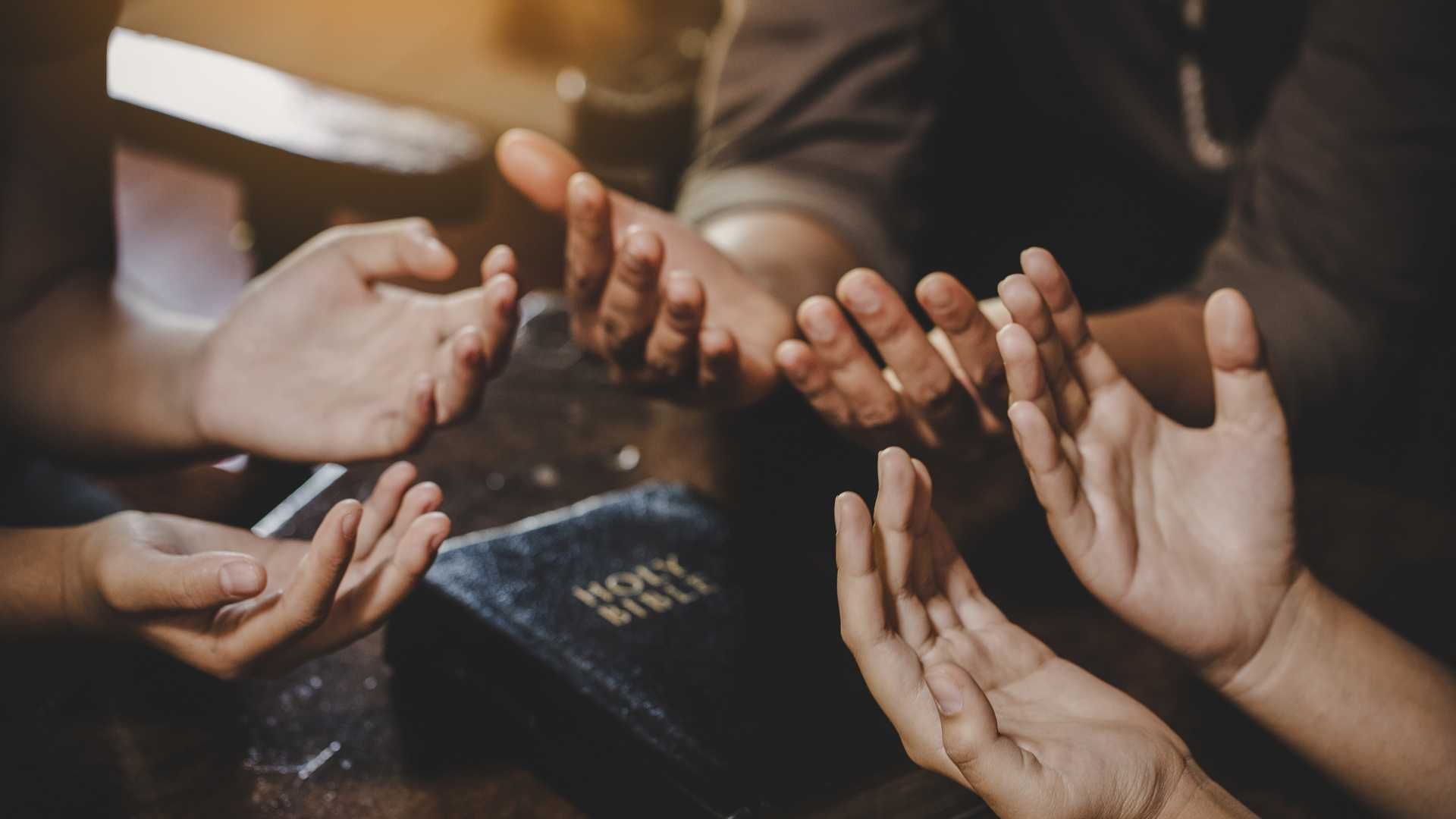 three pairs of open hands facing palm up around a bible