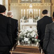 4 men carrying a casket with a flower arrangement on top