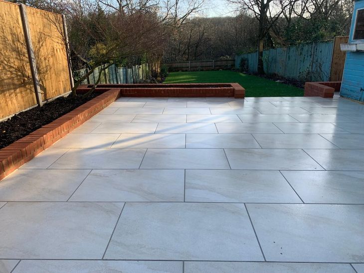 Newly paved patio with light gray stone, red brick edging, and a brick wall.