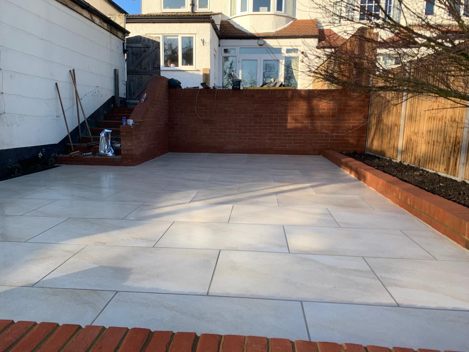 Newly paved patio with light gray stone, red brick edging, and a brick wall.