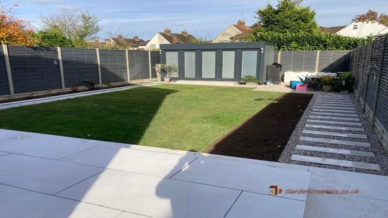 A backyard with a fence and a lawn with paths & borders.