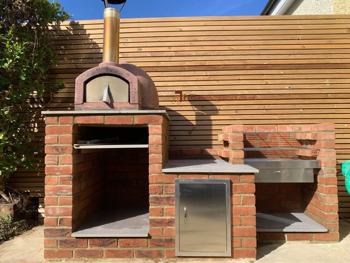 A brick-built outdoor kitchen featuring a pizza oven, a stainless steel storage cabinet, and a built-in barbecue grill.