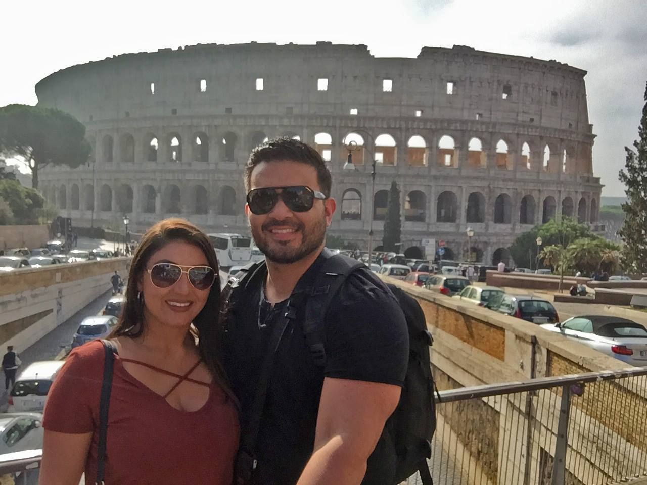 A man and a woman are posing in front of the colosseum