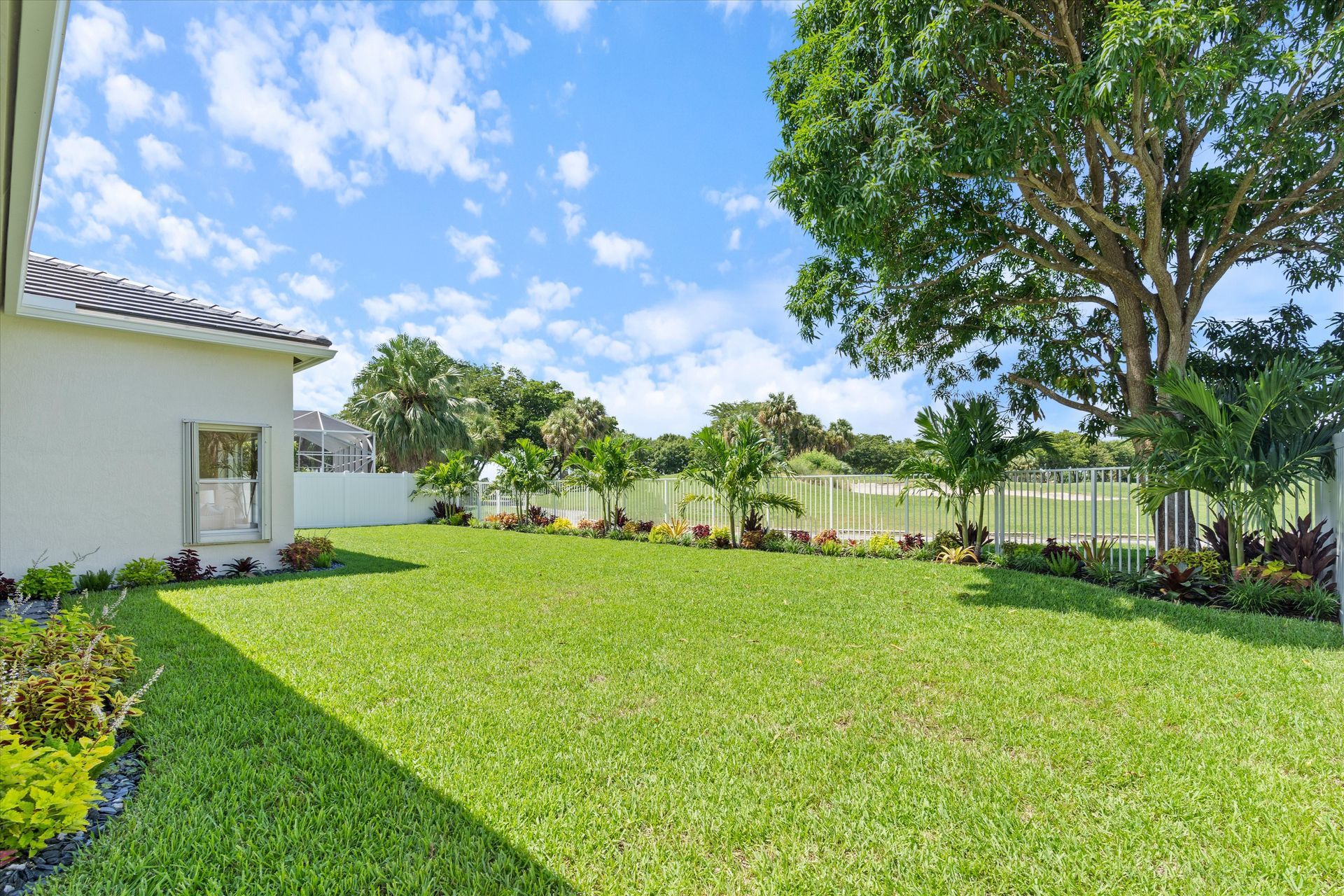 The backyard of a house with a large lush green lawn and trees.