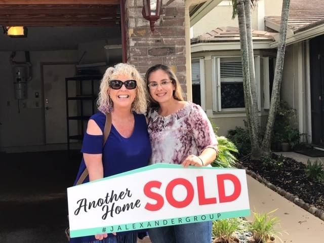 Two women holding a sold sign in front of a house